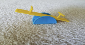 The picture is a close-up picture of a child's toy teeter totter on white carpet.