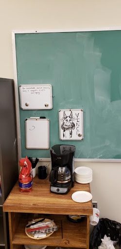 Coffee maker on a table in front of a green chalkboard.