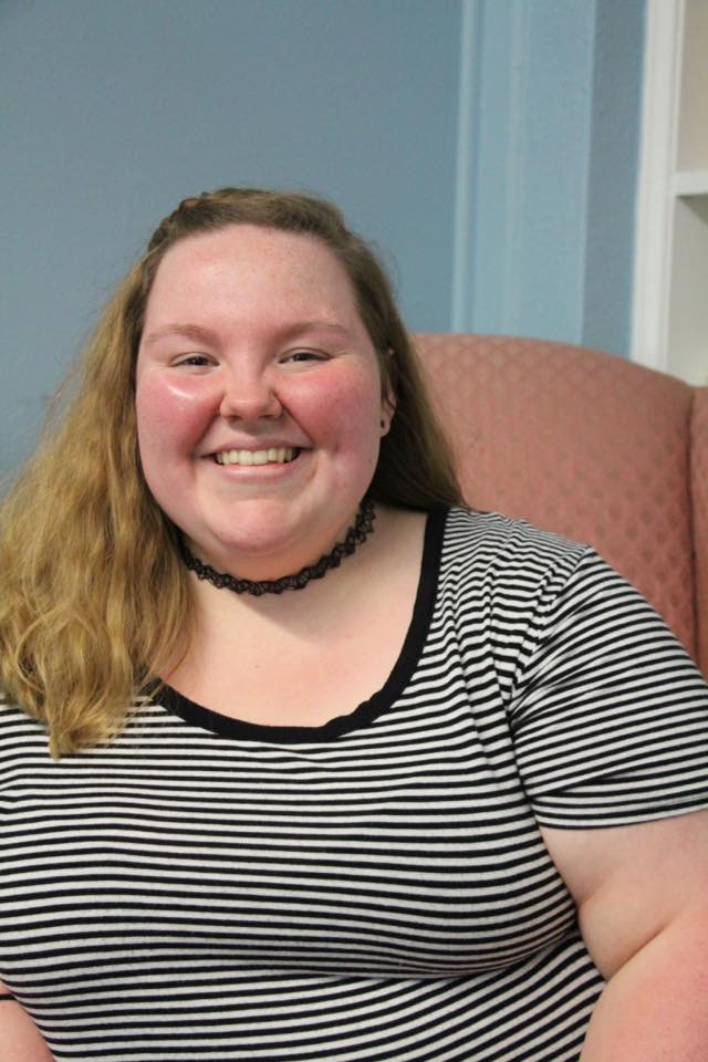 Pender wearing striped dress and seated in a chair.